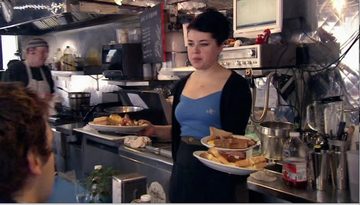 A waitress carrying two plates of food past the line in a small diner kitchen.