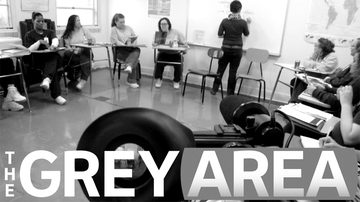 Women seated in a circle of school desks as a facilitator writes on a whiteboard, under the title The Grey Area.