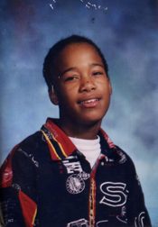 A school portrait of a young boy in a patterned jacket against a blue studio backdrop.
