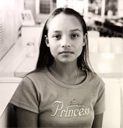 A girl in a T-shirt printed with the word Princess, looking at the camera.