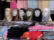 A market stall with headscarves displayed on a row of mannequin heads above stacks of folded fabric.