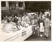 Black-and-white photograph of a crowd gathered behind a car whose side carries a sign reading Daisy Bates.